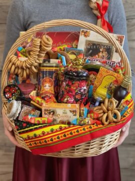 Colorful gift basket filled with chocolates, candies, tea, and a floral teapot, wrapped with decorative red ribbon.
