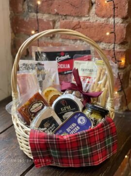 Gift basket filled with assorted Russian snacks and treats, wrapped in red plaid cloth on a wooden table against a brick wall.