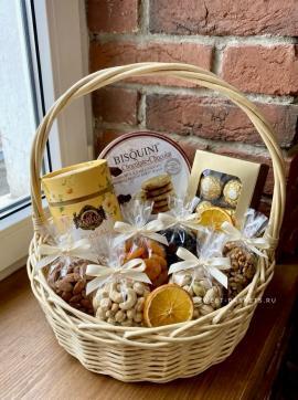 Gift basket with biscuits, chocolates, nuts, dried fruit, and orange slices on a brick windowsill/wood surface.